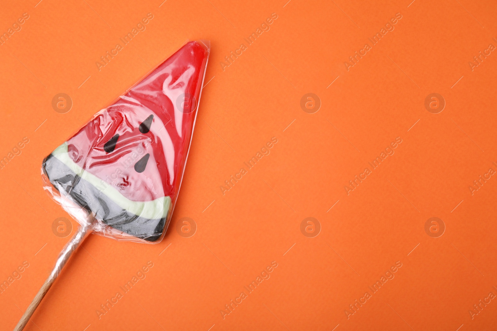 Photo of Watermelon shaped lollipop on orange background, top view. Space for text