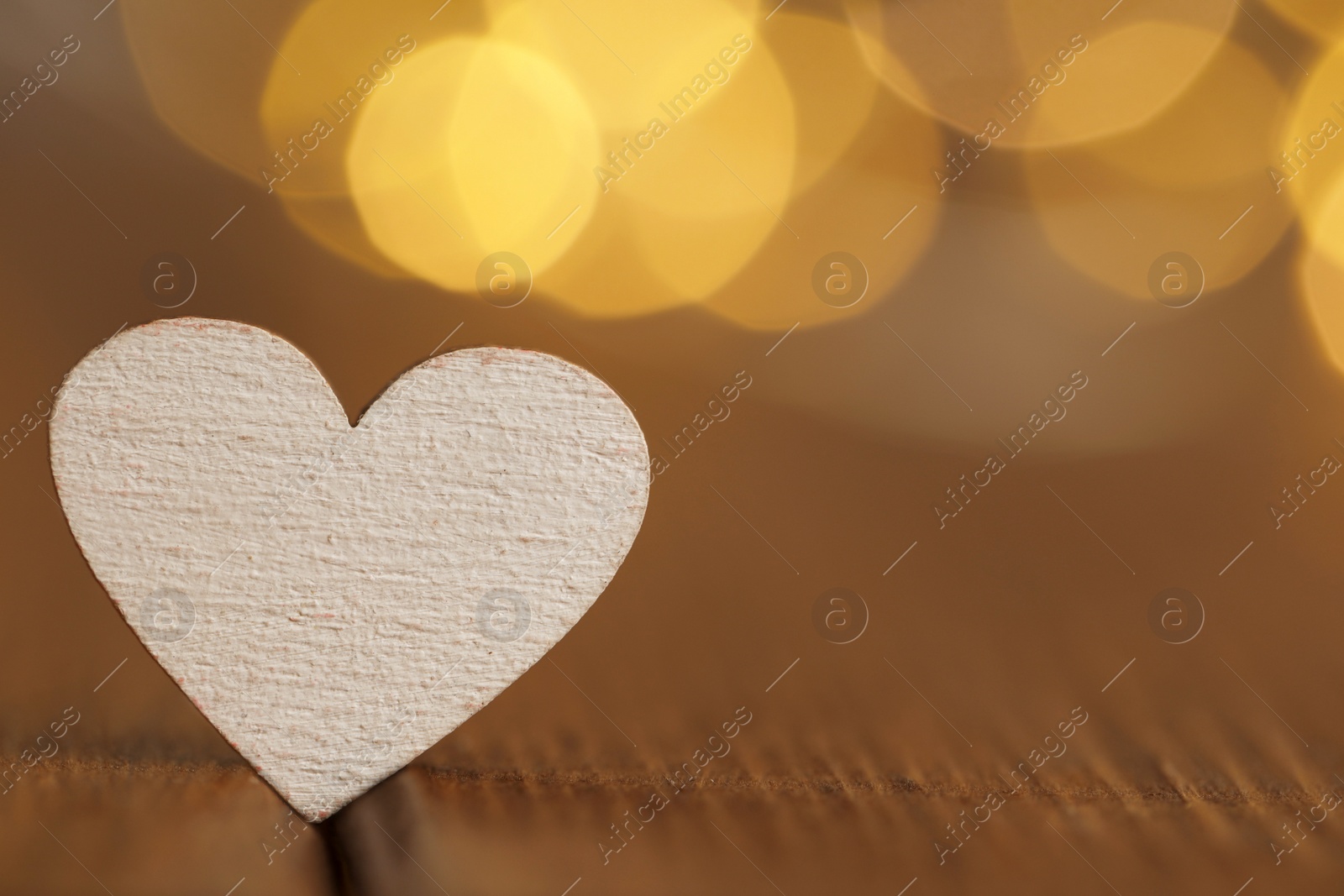 Photo of White heart on wooden table against festive lights, space for text. St. Valentine's day