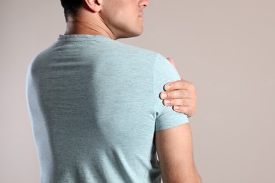 Photo of Man suffering from shoulder pain on beige background, closeup