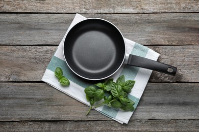 Frying pan and fresh basil on wooden table, top view