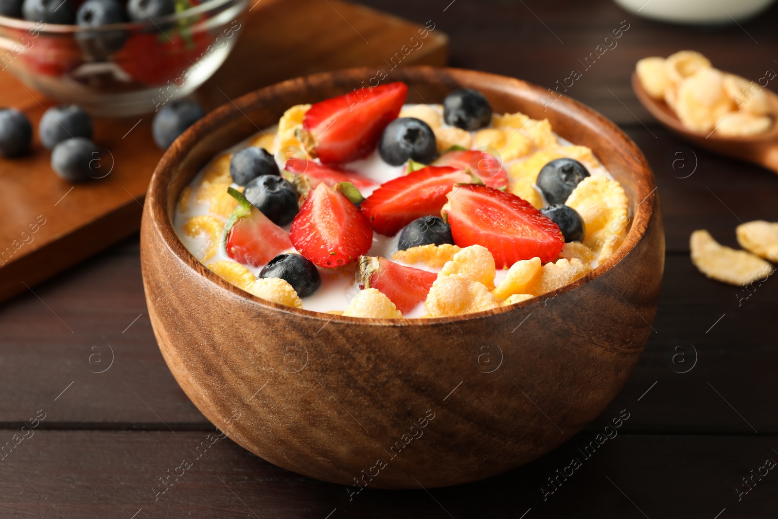 Photo of Bowl of tasty crispy corn flakes with milk and berries on wooden table, closeup