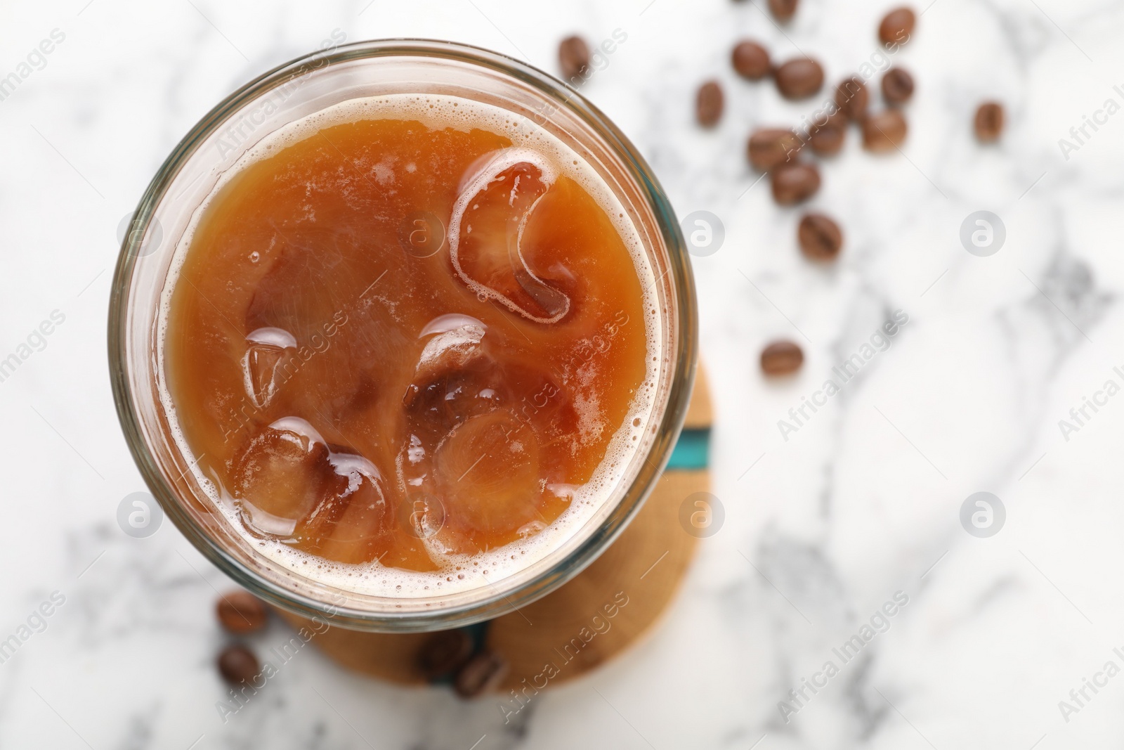 Photo of Refreshing iced coffee with milk in glass and beans on white marble table, top view. Space for text