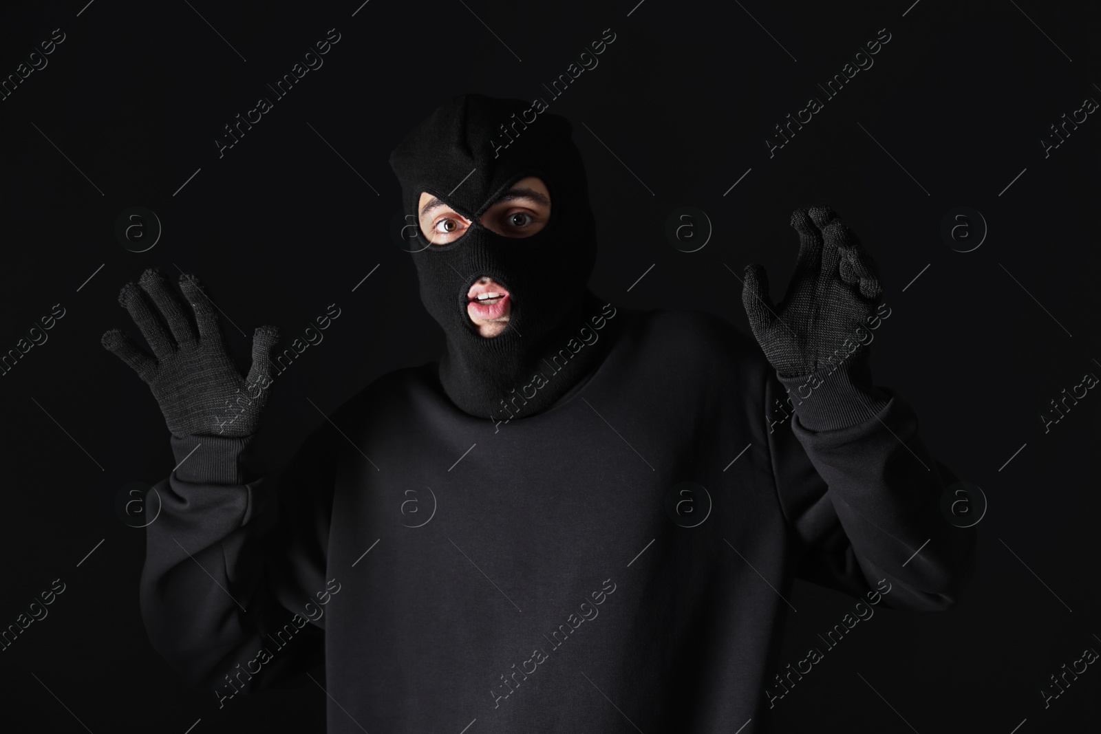 Photo of Thief in hoodie raising hands against black background
