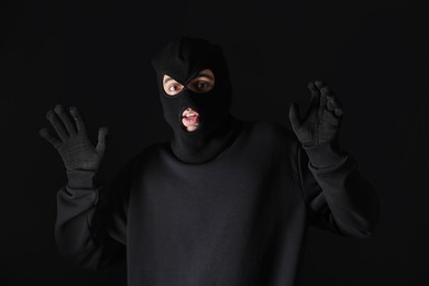 Thief in hoodie raising hands against black background