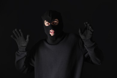 Photo of Thief in hoodie raising hands against black background