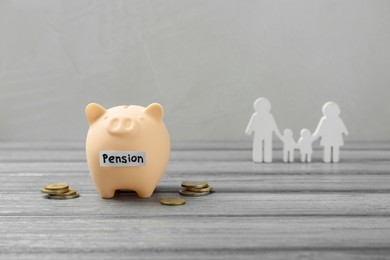 Photo of Pension savings. Piggy bank, coins and figures of family on grey wooden table, space for text