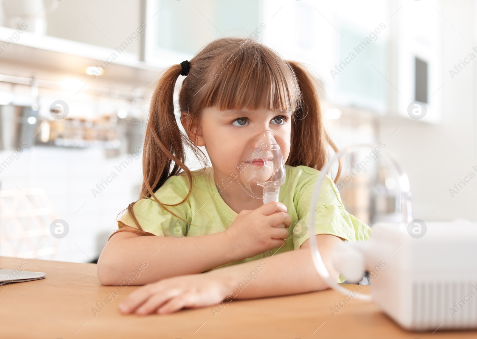 Photo of Little girl using asthma machine at table in kitchen