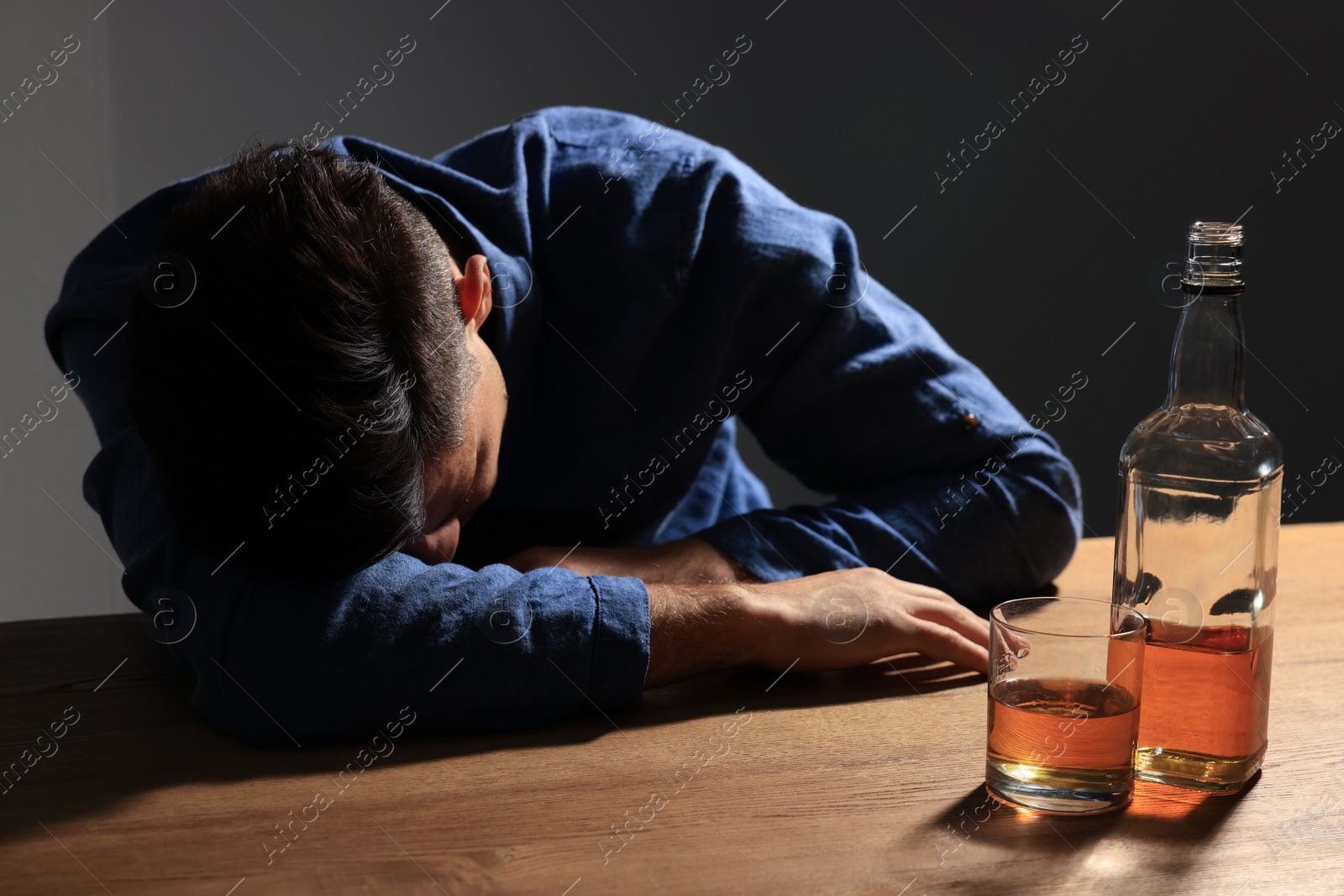 Photo of Addicted man with alcoholic drink at wooden table indoors