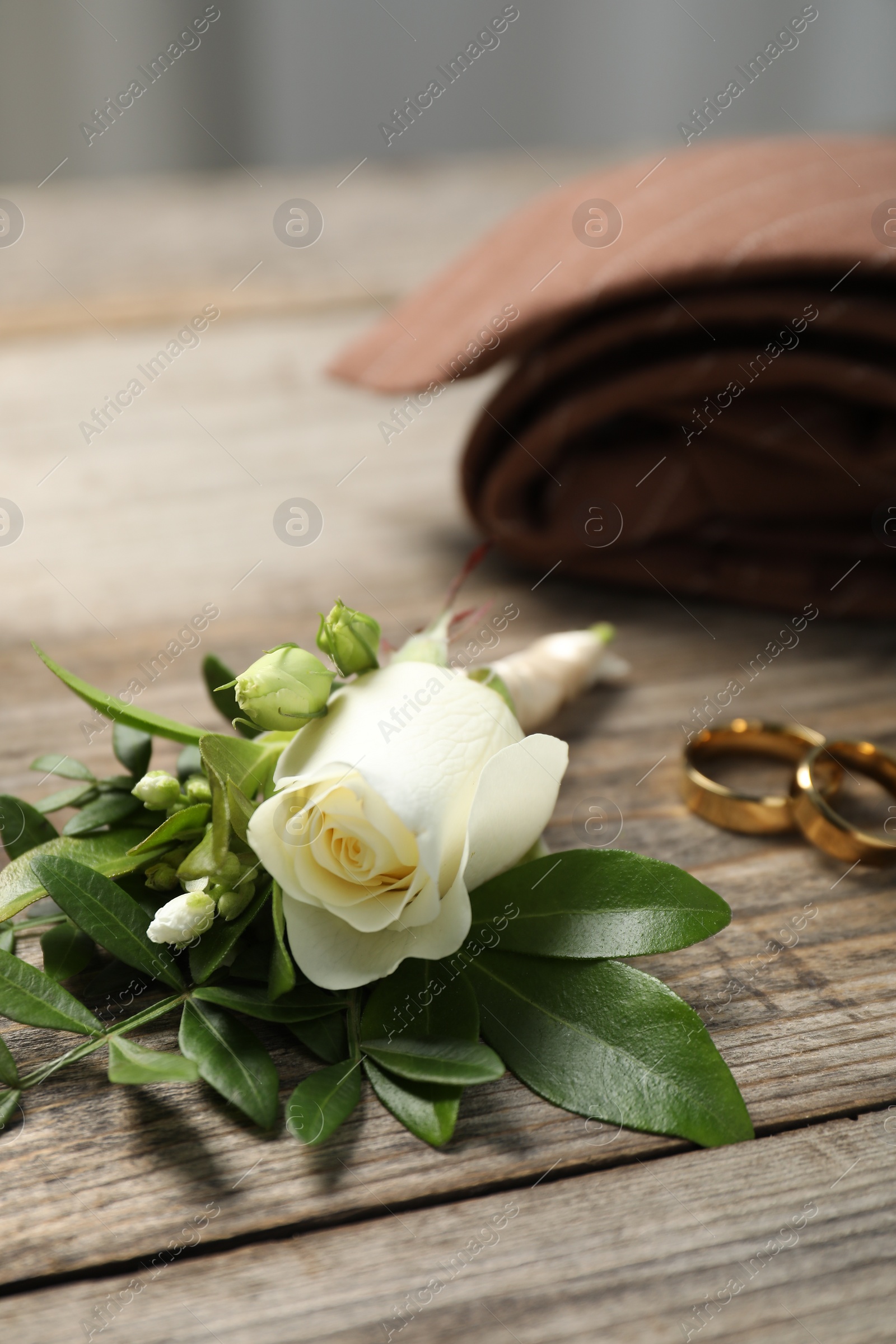 Photo of Wedding stuff. Stylish boutonniere, tie and rings on wooden table, closeup