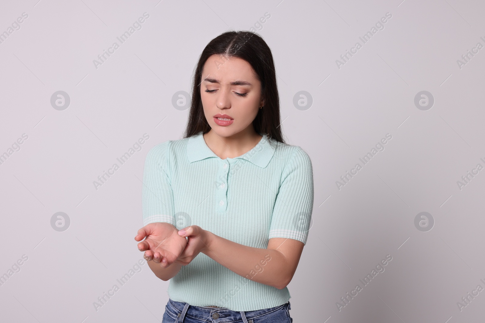 Photo of Young woman suffering from pain in hands on light grey background. Arthritis symptoms