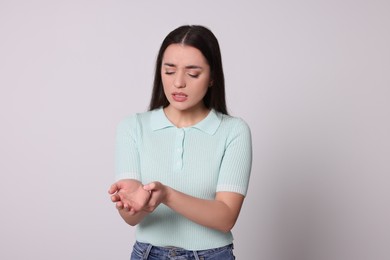 Young woman suffering from pain in hands on light grey background. Arthritis symptoms