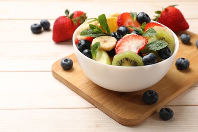 Tasty fruit salad in bowl and ingredients on wooden table, closeup. Space for text