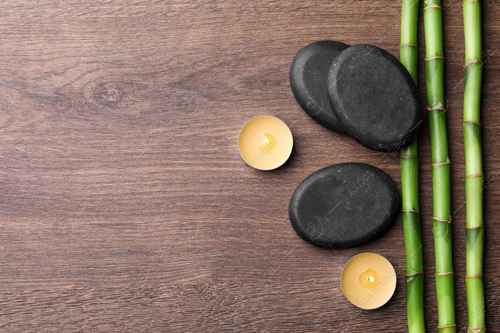 Photo of Spa stones, burning candles and bamboo stems on wooden table, flat lay. Space for text