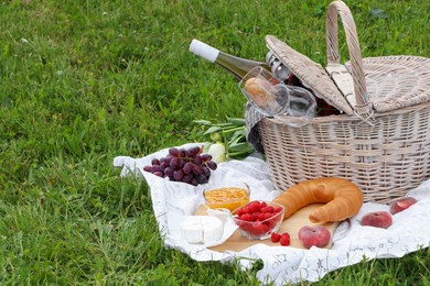 Photo of Picnic basket with tasty food, flowers and cider on blanket outdoors