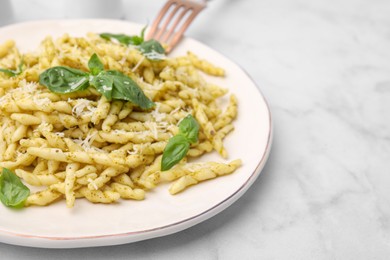 Photo of Plate of delicious trofie pasta with pesto sauce, cheese and basil leaves on white marble table, closeup. Space for text