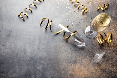 Champagne glasses and serpentine streamers on grey table, view from above. Space for text