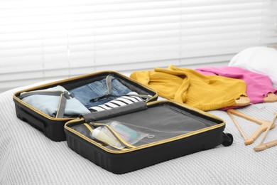 Photo of Plastic bag of cosmetic travel kit in suitcase and clothes on bed indoors. Bath accessories