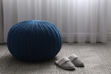 Photo of Stylish blue pouf and slippers on floor in room, space for text