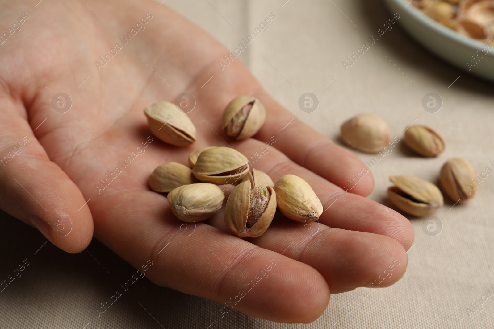 Photo of Woman holding tasty roasted pistachio nuts at table, closeup