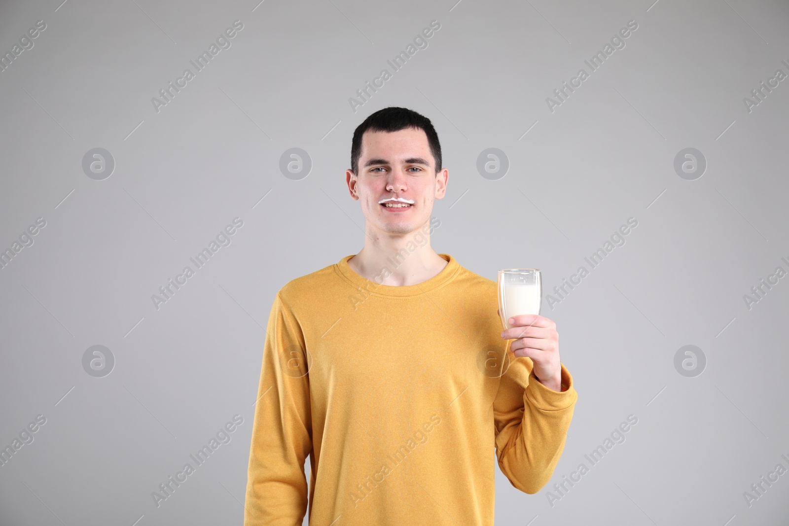 Photo of Happy man with milk mustache holding glass of tasty dairy drink on gray background