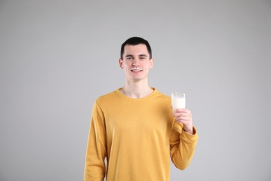 Happy man with milk mustache holding glass of tasty dairy drink on gray background