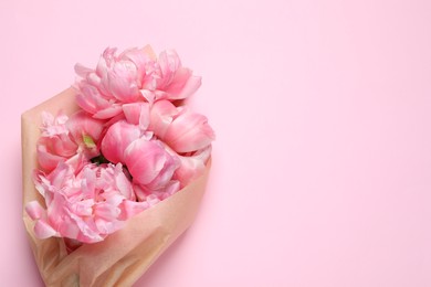 Beautiful bouquet of peonies wrapped in paper on pink background, top view. Space for text