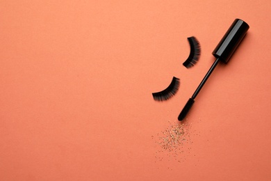 Photo of False eyelashes and mascara on orange background, flat lay. Space for text