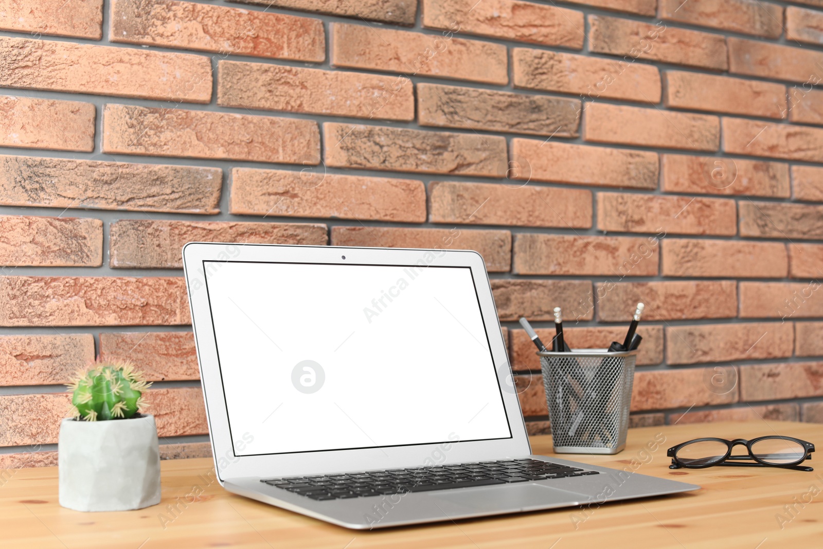 Photo of Modern laptop on table against brick wall. Mock up with space for text