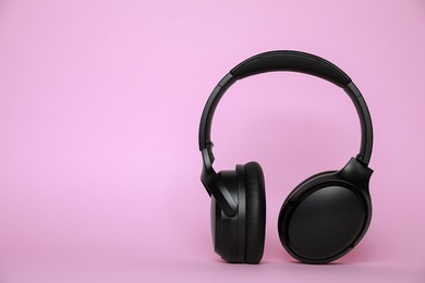 Photo of Modern wireless headphones on pink background. Space for text