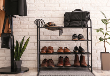 Photo of Shelving rack with stylish shoes and accessories near white brick wall indoors