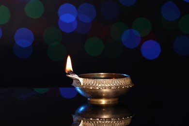 Lit diya on dark background with blurred lights, space for text. Diwali lamp