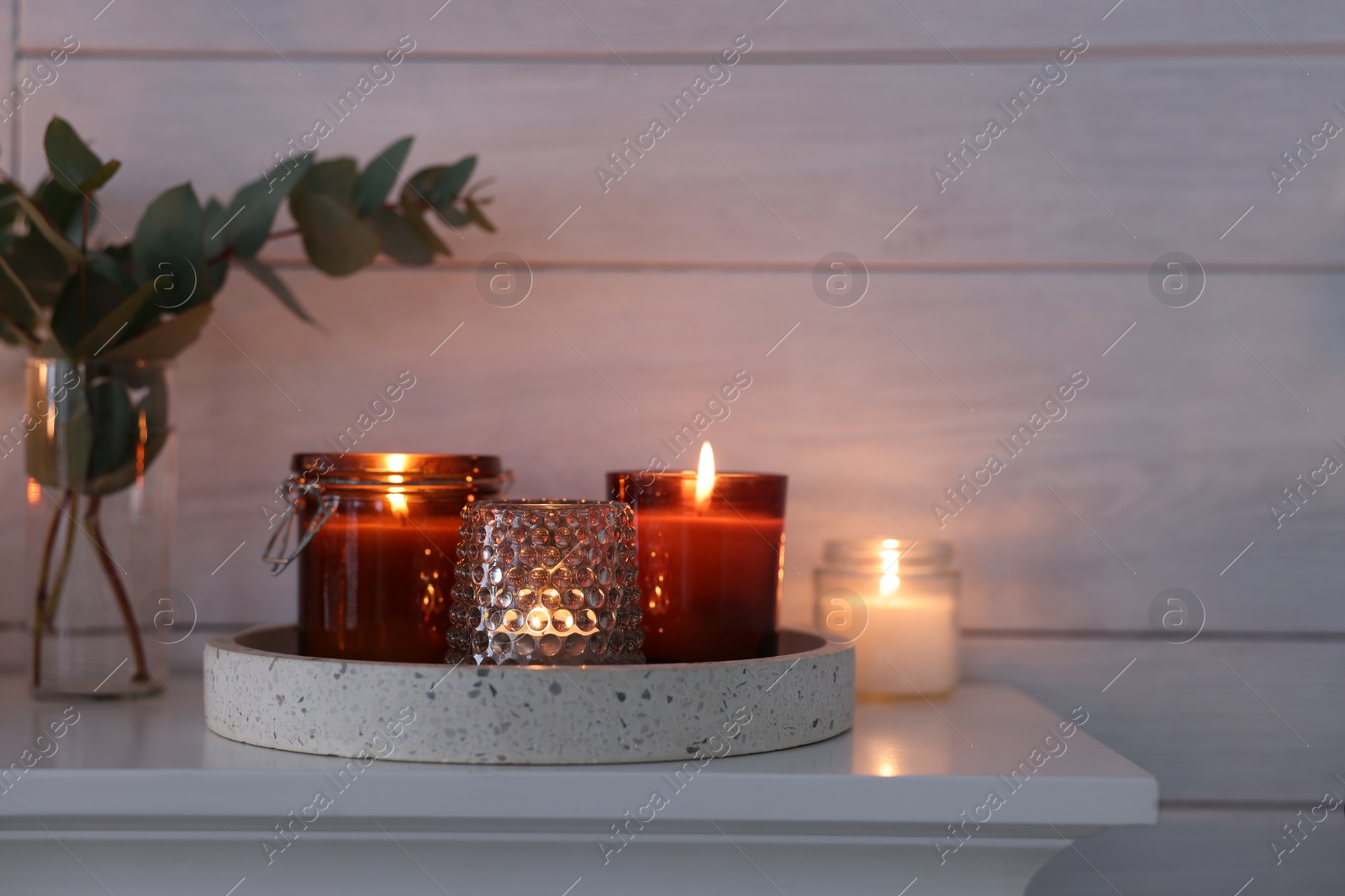 Photo of Burning candles on mantel near white wall indoors