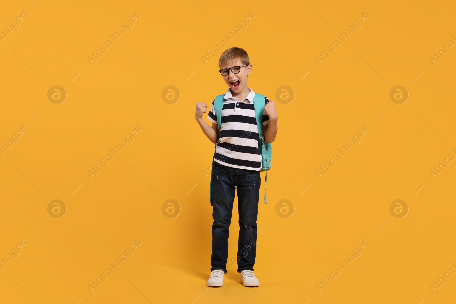 Photo of Emotional schoolboy in glasses with backpack on orange background