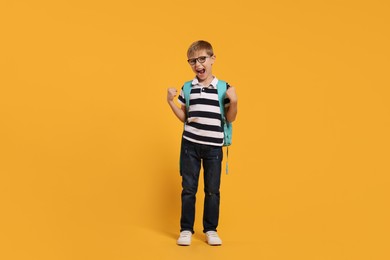Photo of Emotional schoolboy in glasses with backpack on orange background