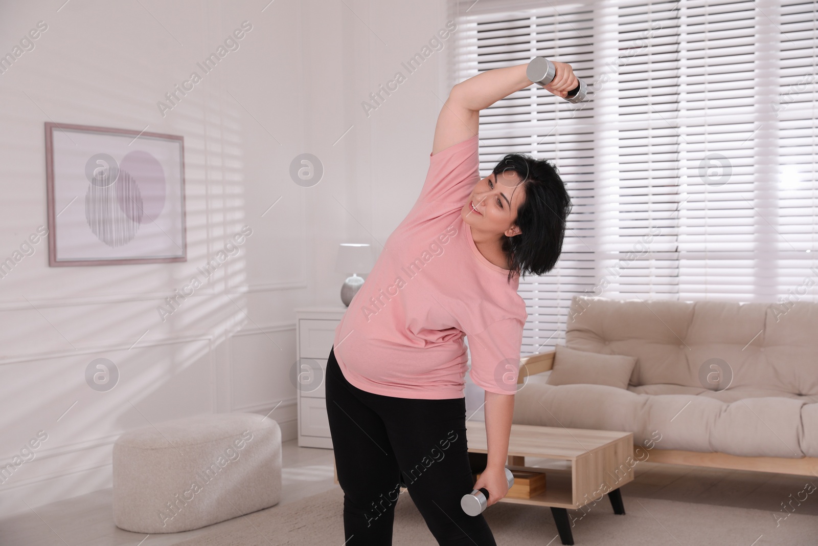 Photo of Overweight mature woman doing exercise with dumbbells at home