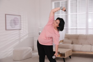 Overweight mature woman doing exercise with dumbbells at home