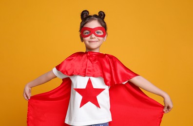 Photo of Cute little girl in superhero suit on yellow background