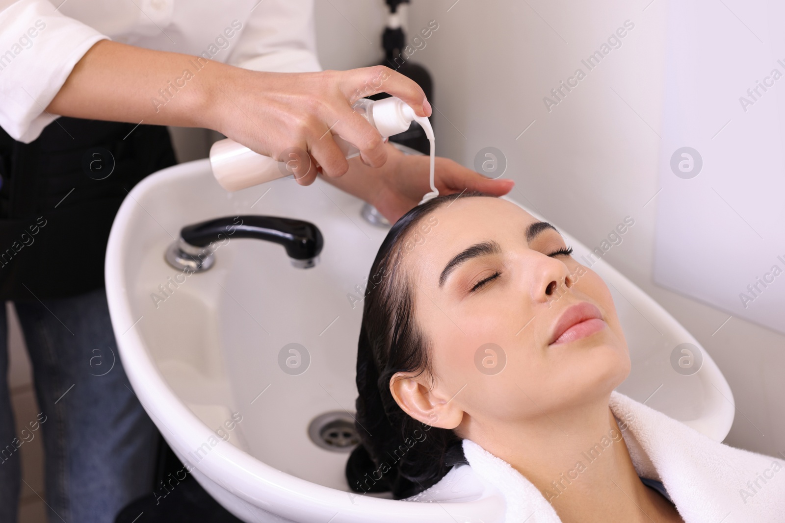 Photo of Professional hairdresser washing woman's hair in beauty salon, closeup