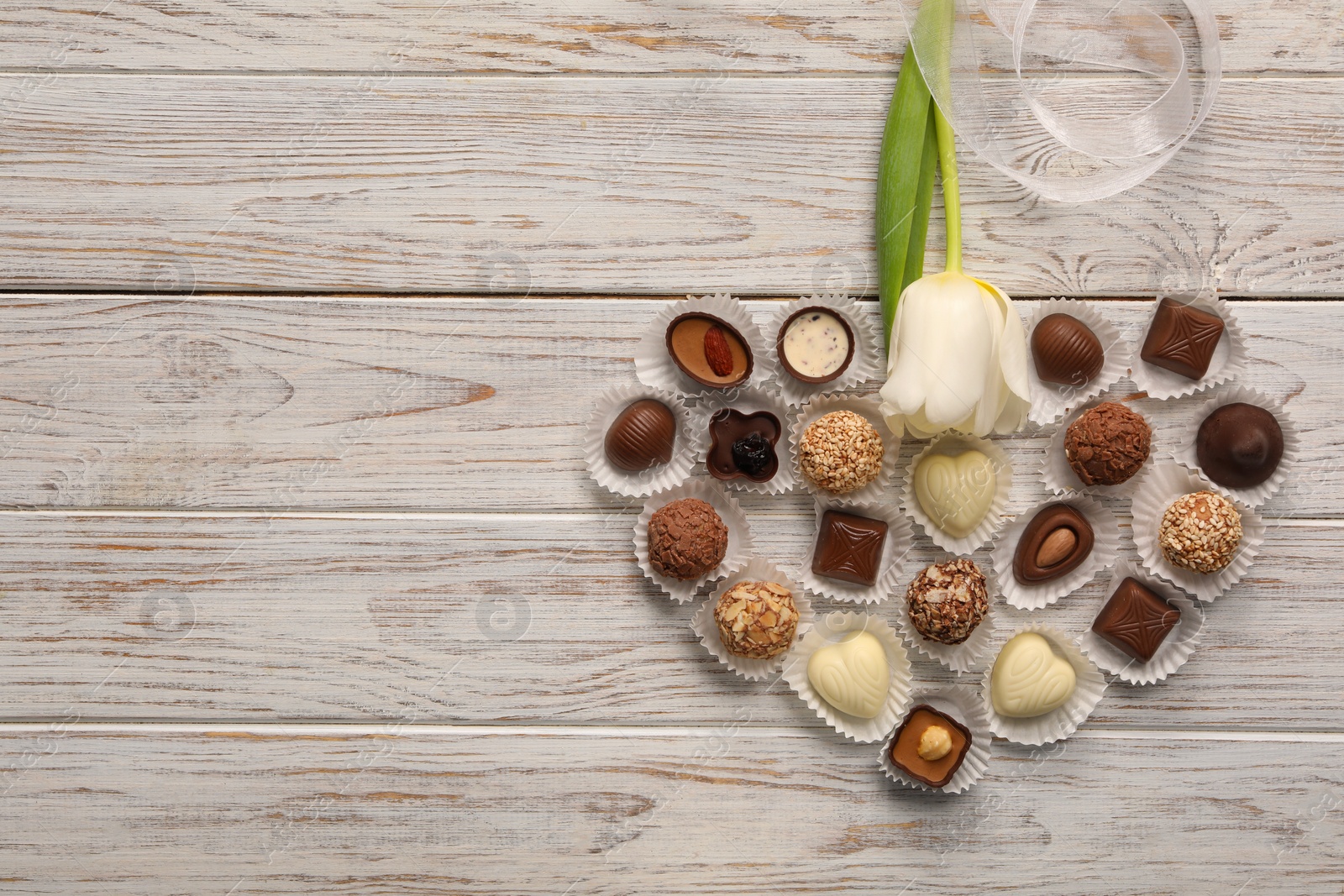 Photo of Heart made with delicious chocolate candies and beautiful tulip on white wooden table, flat lay. Space for text