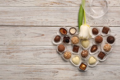 Photo of Heart made with delicious chocolate candies and beautiful tulip on white wooden table, flat lay. Space for text