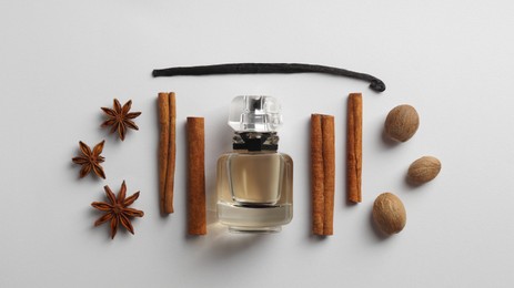 Photo of Bottle of perfume surrounded by different spices on white background, top view