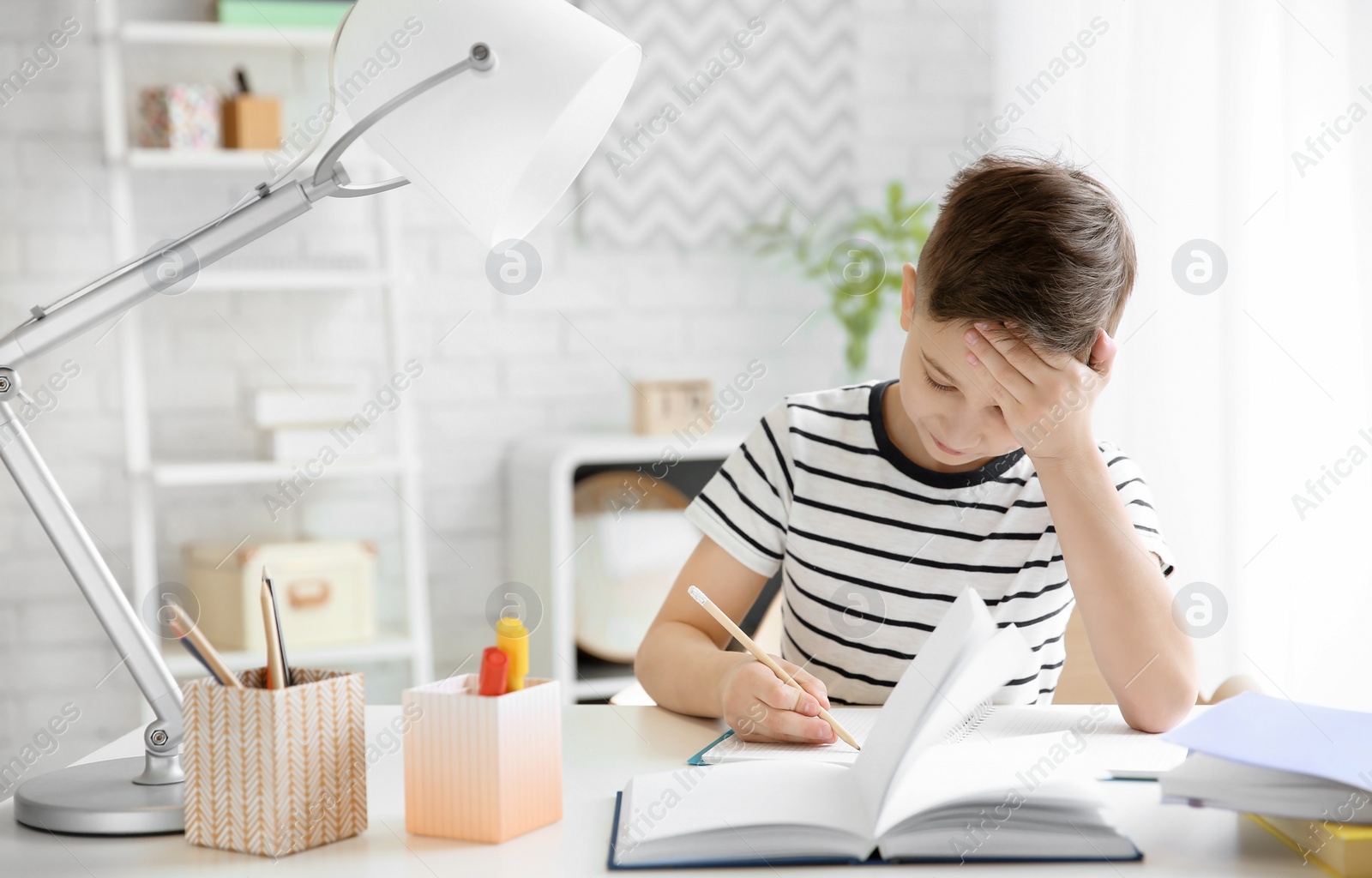 Photo of Little boy suffering from headache while doing homework at table indoors