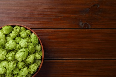 Photo of Bowl with fresh green hops on wooden table, top view. Space for text