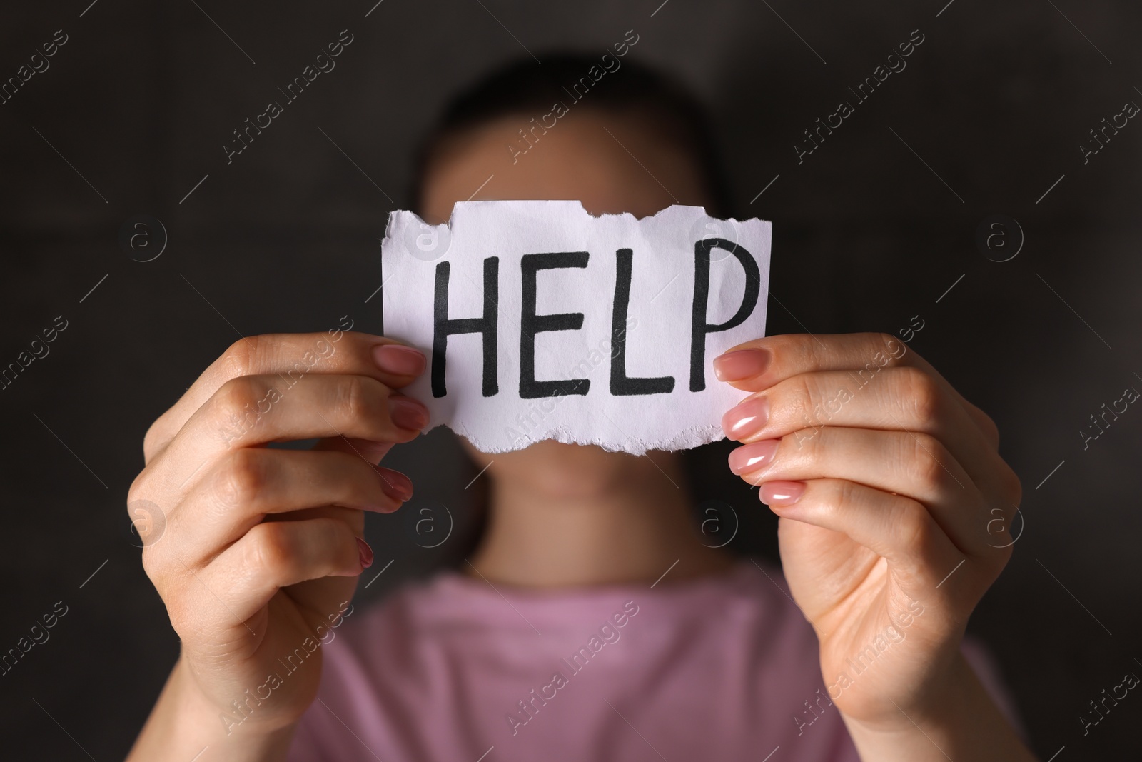 Photo of Woman holding piece of paper with word Help on dark background, closeup. Domestic violence concept