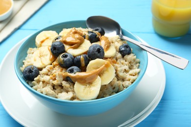 Photo of Tasty oatmeal with banana, blueberries and peanut butter served in bowl on light blue wooden table