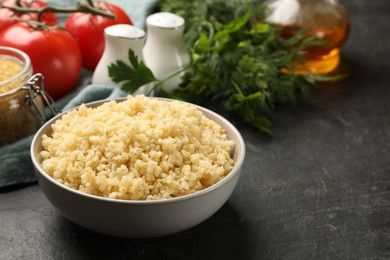 Photo of Delicious bulgur in bowl on black table, space for text