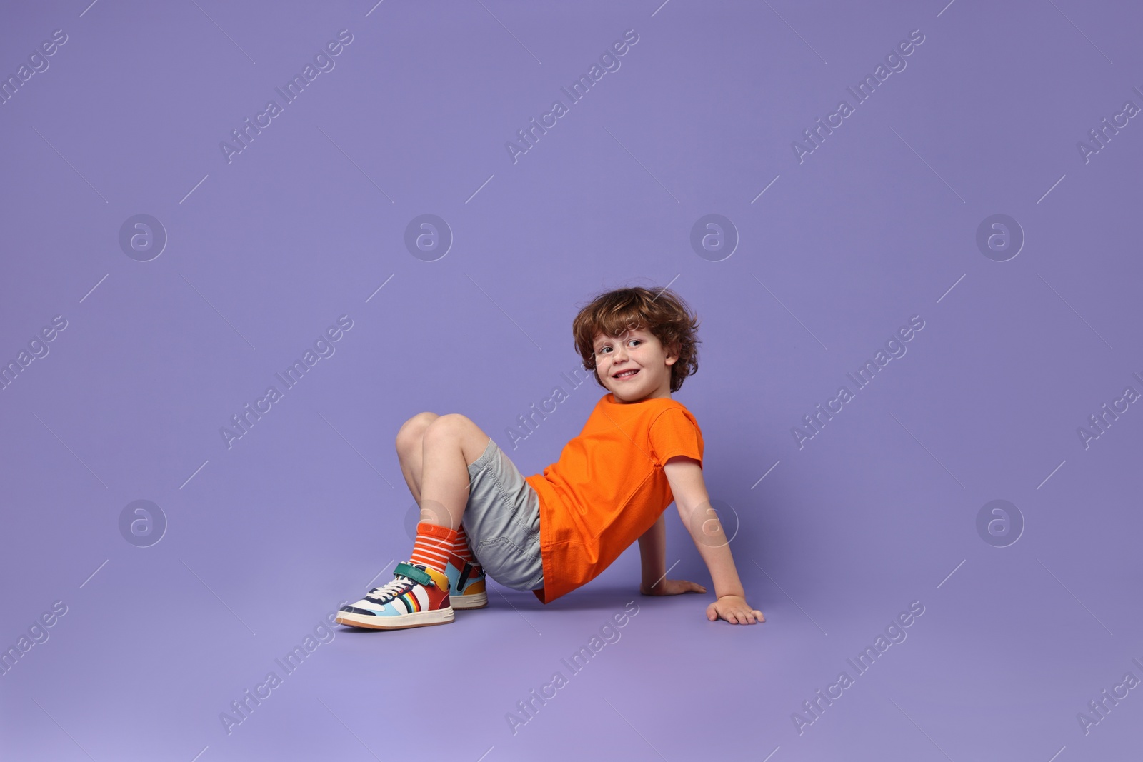 Photo of Happy little boy dancing on violet background