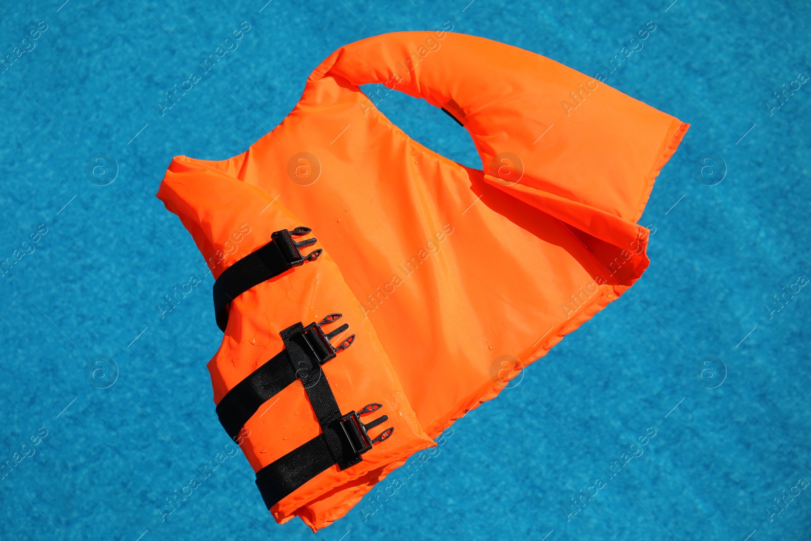 Photo of Bright orange life jacket floating in swimming pool, top view