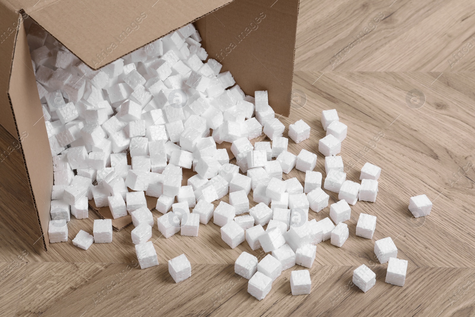 Photo of Overturned cardboard box with styrofoam cubes on wooden floor