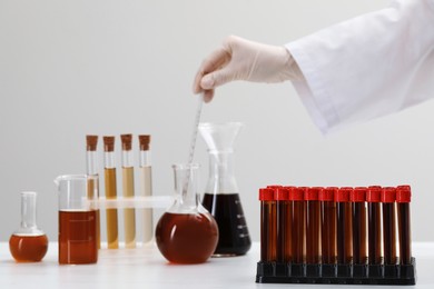Photo of Scientist mixing brown liquid in round bottom flask at table, focus on test tubes